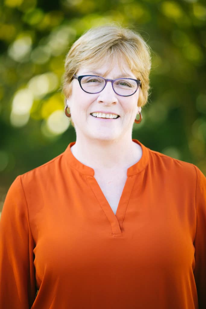 A woman in an orange shirt smiling for the camera.